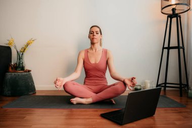 Güzel sarışın kadın evde antrenman yapıyor. Kadın evde yoga yapıyor. Sağlıklı ve aktif yaşam tarzı için egzersiz dersleri alan formda bir kız. Kadın evde çalışmak için karantina kullanıyor. Evimde geriniyorum