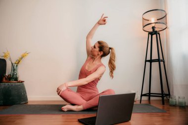 Güzel sarışın kadın evde antrenman yapıyor. Kadın evde yoga yapıyor. Sağlıklı ve aktif yaşam tarzı için egzersiz dersleri alan formda bir kız. Kadın evde çalışmak için karantina kullanıyor. Evimde geriniyorum