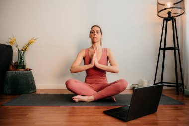 Güzel sarışın kadın evde antrenman yapıyor. Kadın evde yoga yapıyor. Sağlıklı ve aktif yaşam tarzı için egzersiz dersleri alan formda bir kız. Kadın evde çalışmak için karantina kullanıyor. Evimde geriniyorum
