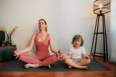 Genç anne ve oğlu evde yoga yapıyor. Sabahları çocuk egzersizi yapan sportif bir anne. Anne ve oğlu egzersizleri birlikte yapıyor, sağlıklı bir aile hayatı. Coronavirus evde kal. COVID-19 tarafından acil kapatma.