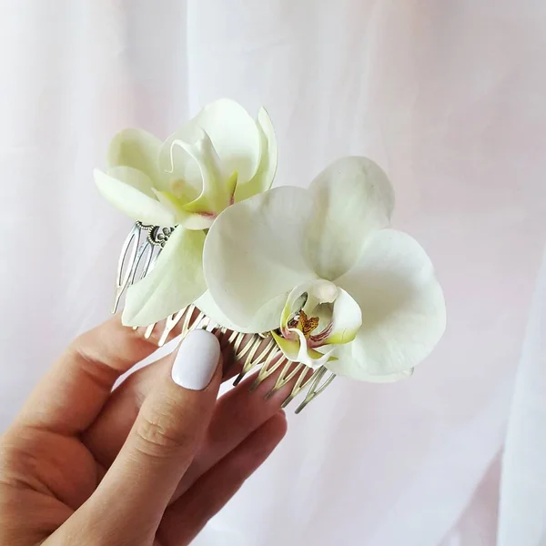 Bu, taze beyaz çiçek desenli bir dekorasyonun fotoğrafı. Çiçeklere falaenopsis denir. Bir el, düğün görüntüsü için bir tarak tutar..