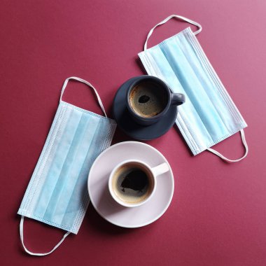 Cerrahi kulak maskesi ve şarap rengi arka planda bir fincan kahve. Tıbbi maske kraliyet virüsüne veya COVID-19 karantinasına karşı korur. Biyolojik hayat kavramı. Yaşam tarzı ve Yassı Yatay.