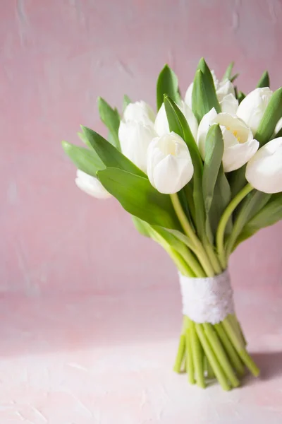 This is a bouquet of white tulips. The handle of the bunch is decorated with cotton lace. Vintage pink background . The gamma of the foto consists of white and powdery pink colors.