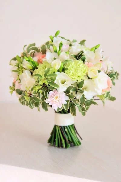 A bouquet of mint and peach colors is on the table. It consists of white freesia, green dianthus, peach roses, light chrysanthemum and fresh greens. Bouquet for the bride or girl.