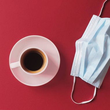 Koruyucu tıbbi maske ve kahve fincanı kırmızı masada. Bakterilerin prosedür maskesi. Coronavirus çağındaki yaşam konsepti. Yaşam biçimi