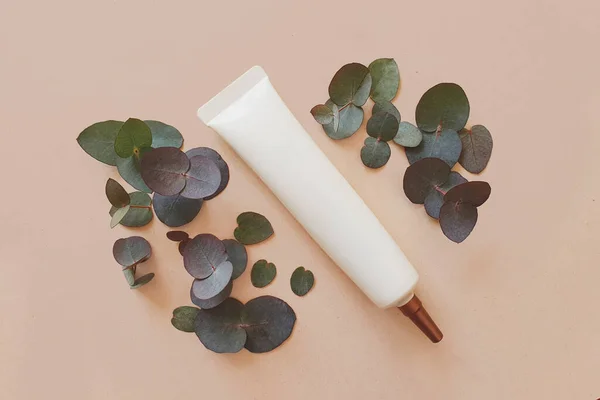 Yüz kremi sıkma, uzun hortumlu kozmetik tüp ve bronz vida kapağı. Model-up. Yeşil okaliptüslü el işi arka plan. Metin için boşluk