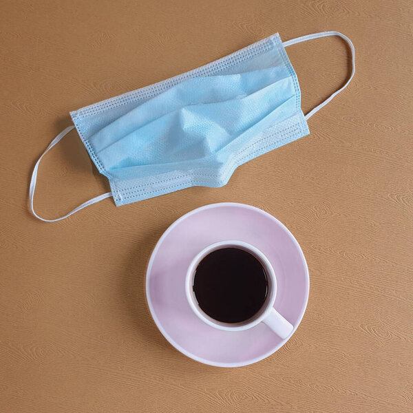чашка с кофе и защитная медицинская маска находятся на деревянном столе. Вид сверху, место для текста
. 