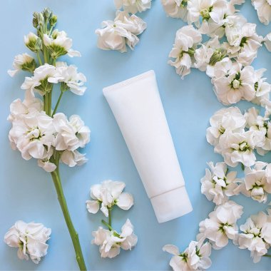 Güzellik spası tıbbi cilt bakımı ve kozmetik losyon şişesi krem ambalaj ürünleri soluk mavi arka planda beyaz çiçeklerle birlikte. Genel bakış. Çiçekli düz yatak, yaşam tarzı. Temiz güzellik kavramı