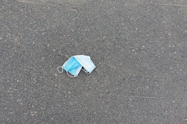 Çöpe atılmış bir tıbbi maske yolda yatıyor. Bulaşıcı kişisel koruyucu ekipmanların imhası sorunu. 
