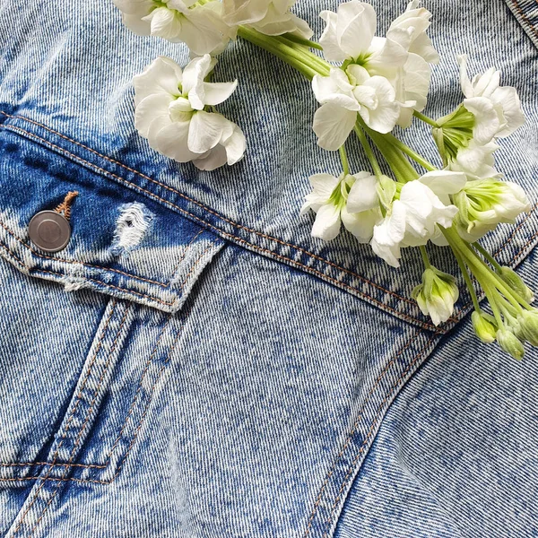 Textile denim background and flowering white branch. Pocket blue denim jacket.  Product background. This is the place for your beauty products and text. View from above.