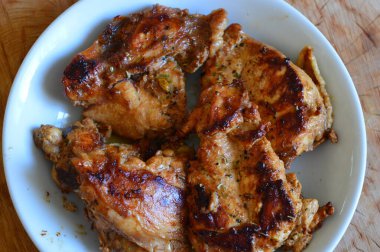 Ahşap bir masada ızgara tavuk budu ve beyaz tabak.