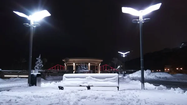 Gece kentinde karla kaplı bir bank.