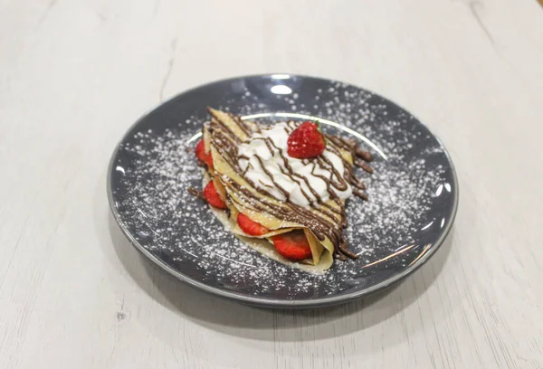 Crepe with chocolate, strawberrys and whipped cream on gray plate