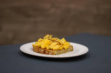 Mavi masadaki beyaz tabakta çırpılmış yumurta tostu ve ahşap arka plan.