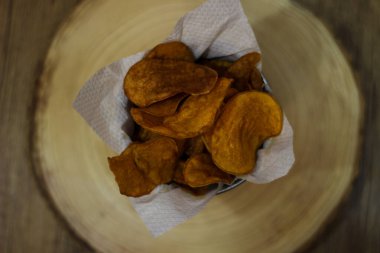 Patates cipsi kızartması beyaz peçeteli ve ahşap arka planda üst kasede görülüyor.