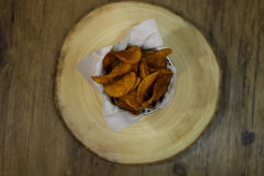 Patates cipsi kızartması beyaz peçeteli ve ahşap arka planlı bir kasede en üst görüntüde.