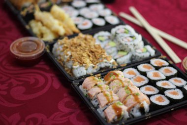 Somon, Hosomaki, California, URAMAKI, kızarmış soğan, kızarmış soğan, haşlanmış somon, bir kase acı tatlı, tatlı ve ekşi sos, kırmızı masa örtüsünde çubuk.