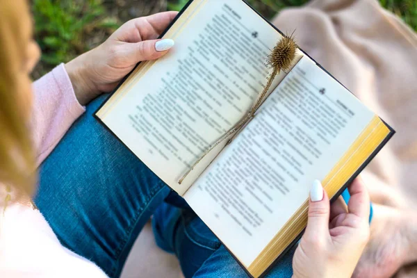 Foto morbida di una giovane ragazza, bionda, leggere un libro, vista dall'alto. Seduto nel giardino primaverile su una coperta leggera, in abiti di tutti i giorni. Primavera. Giorno . — Foto Stock