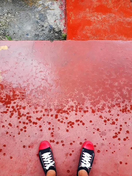 Feet with shoes on red ground with raindrops on the street