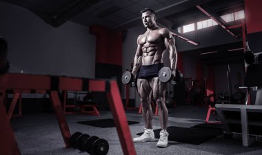 kaslı vücut geliştirmeci biri dumbbells ile yapıyor