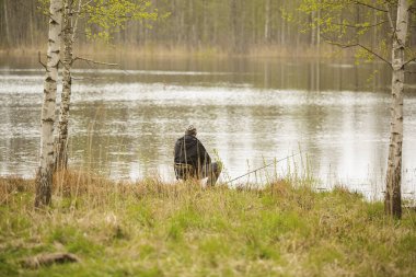 Balıkçı elinde oltayla gölün kıyısında oturur.