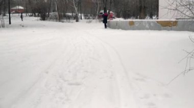 Yoldan geçen biri oyun alanının önünden geçiyor. Kar yağıyor. Ağacın arkasından bir adam gözleniyor..