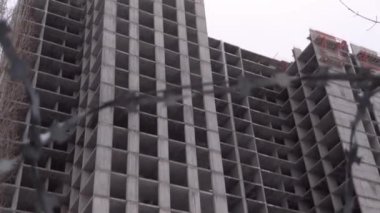 Terk edilmiş inşaat alanı. Çitin arkasından bir bakış. Dikenli tel. İnşaat durdu. Tamamlanmamış gri bina.