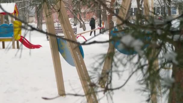通行人が遊び場を通り過ぎる 雪が降ってる 木の後ろから男の観察 — ストック動画