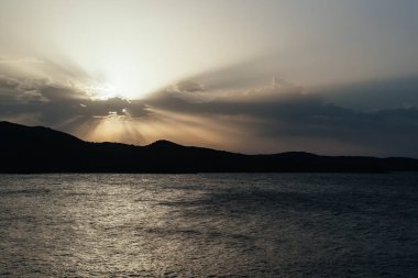 Gün batımında bulutlar ve ufukta bir ada arasında