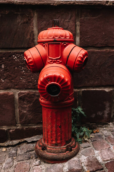 Old red rusty cast iron fire hydrant with rustic brown stone background and cobblestone floor