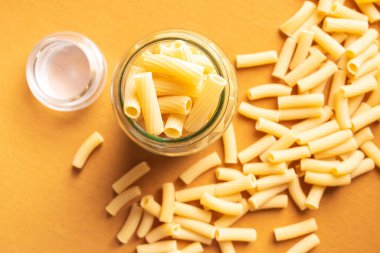 Konserve kavanozu turuncu zemin üzerinde rigatoni makarnası ve odaksız badem kurabiyesi ve Swabian ışığı ile dolu.