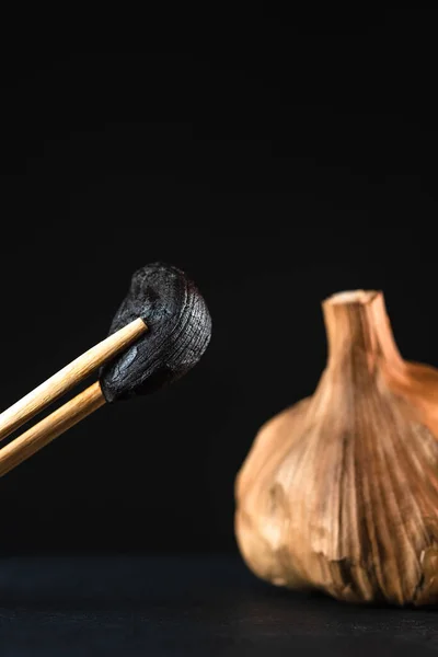 macro photography of black garlic clove with chopsticks, garlic head and black background.
