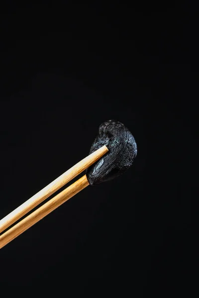 macro photography of black garlic clove with chopsticks and black background.