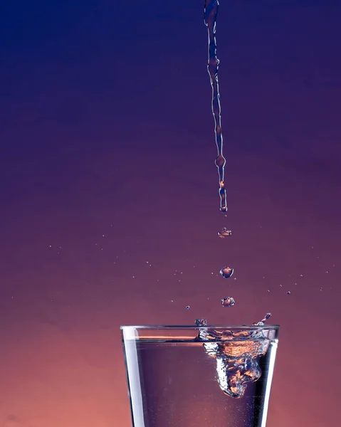 Detail of water splashing into a glass with purple background.