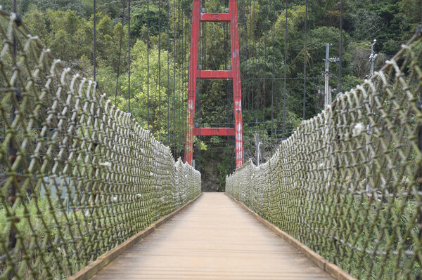 Wooden suspension bridge with a metal fence and red arch.