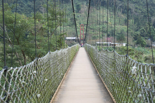 Wooden suspension bridge with a metal fence and red arch.