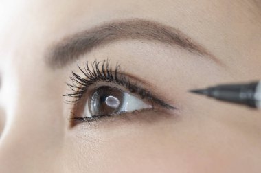 Beyaz arka planda göz kalemi kullanan genç bir kadının portresi