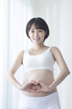 Genç hamile Asyalı kadın, elleri karnında kalp yapıyor..