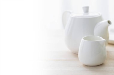 Beyaz çaydanlık ve fincan tahtadan bir masada..
