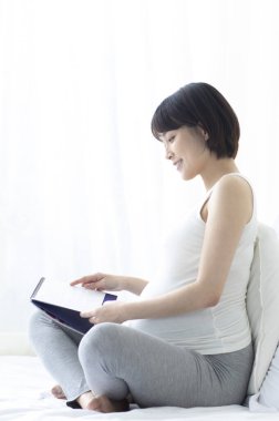 Genç hamile Asyalı kadın yatakta oturuyor ve takvime bakıyor..