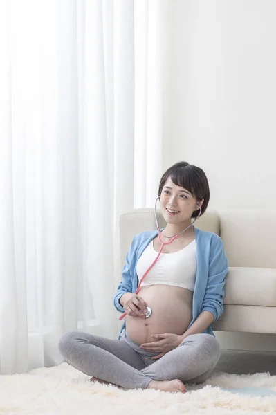 若いです妊娠中のアジアの女性リッスン彼女の赤ちゃんとともに聴診器 — ストック写真