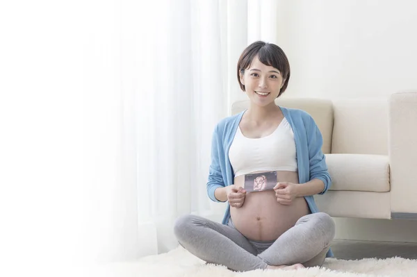 若いです妊娠中のアジアの女性座っていると彼女の赤ちゃんのソノグラムを示します — ストック写真
