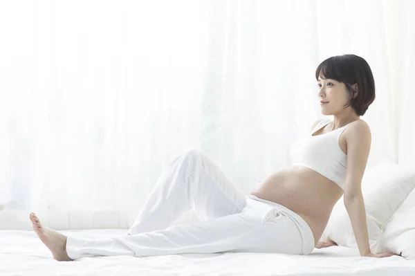 若いです妊娠中のアジアの女性はベッドに座って — ストック写真