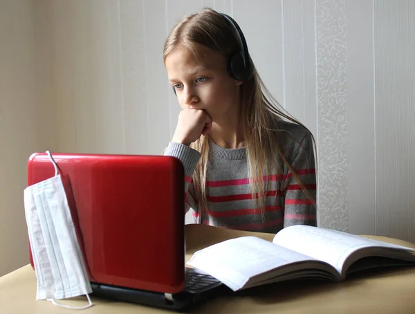 Kulaklıklı sarışın bir ergen kız elinde bilgisayar ve kitapla masada oturuyor. O, biraz yorgun. Evde eğitim. Coronavirus Covid-19 salgını nedeniyle okullar karantinaya alınmıştır. Uzaklık eğitimi.