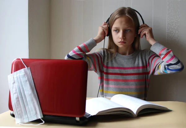 Kulaklıklı sarışın bir ergen kız elinde bilgisayar ve kitapla masada oturuyor. O, biraz yorgun. Evde eğitim. Coronavirus Covid-19 salgını nedeniyle okul karantinaya alınmıştır. Uzaklık eğitimi