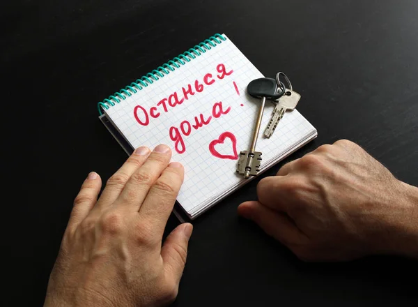 Erkek eli evin anahtarlarını ve üzerinde not olan bir defter tutuyor. Evde Rusça konuş. Koronavirüs Covid-19 salgınından dolayı karantina ya da kendini izole etme. Ev tabelasında kal.