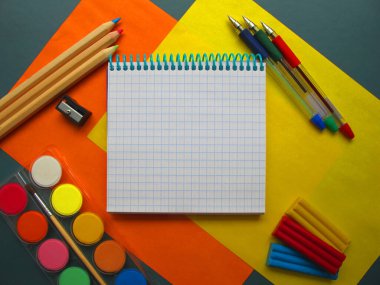 Okul kırtasiyesinin en üst görüntüsü: boyalar, renkli kalemler, kalemler, plastik kalemler ve sarı-turuncu arka plandaki not defteri. Okula geri döndüm. Metnin için boşluk kopyala                       