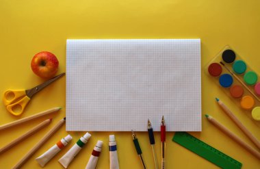 Okul kırtasiyesinin en üst görüntüsü: sarı zemin üzerinde boyalar, renkli kalemler, kalemler, makas, cetvel, not defteri ve elma. Okula geri döndüm. Metnin için boşluk kopyala