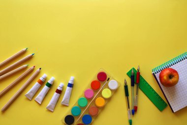 Okul kırtasiyesinin üst görüntüsü: boyalar, renkli kalemler, kalem, not defteri, cetvel ve elma sarı arka planda. Okula geri döndüm. Metnin için boşluk kopyala