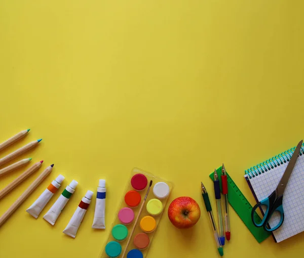 Okul kırtasiyesinin en üst görüntüsü: sarı zemin üzerinde boyalar, renkli kalemler, kalemler, makas, cetvel, not defteri ve elma. Okula geri döndüm. Metnin için boşluk kopyala